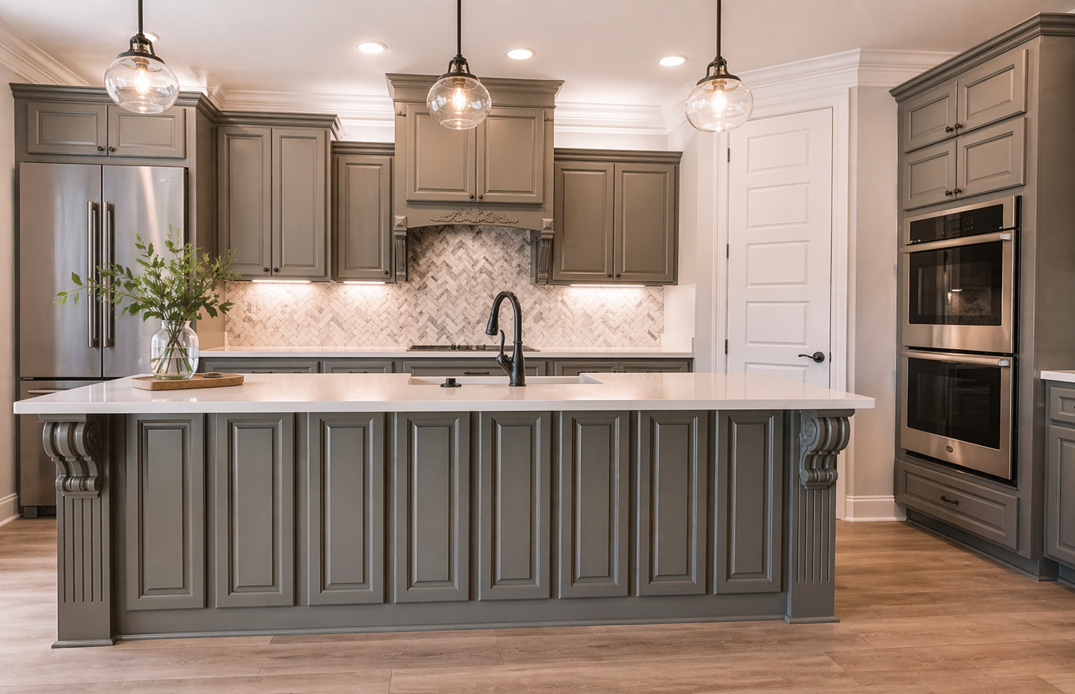Gray solid wood kitchen cabinets with raised panel detailing and a large center island, paired with a light quartz countertop, stainless steel appliances, pendant lighting, and warm-toned luxury vinyl plank flooring in a bright, modern kitchen.